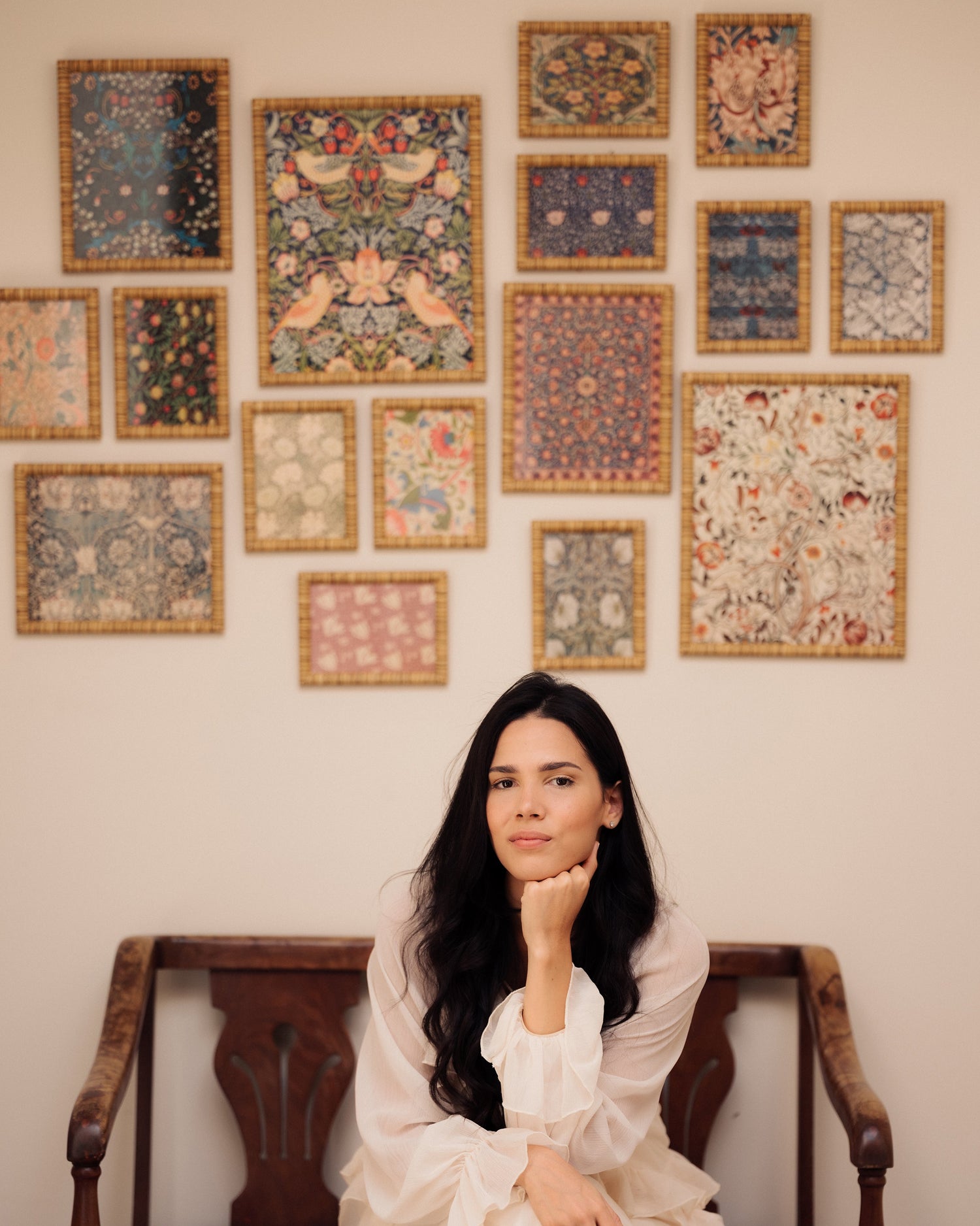Woman in a white dress sitting on a wooden bench with decorative wall art behind her.